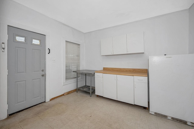 kitchen featuring light countertops, freestanding refrigerator, white cabinetry, and baseboards