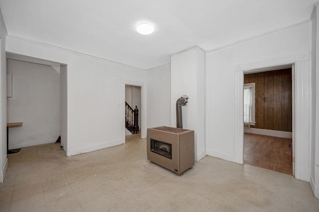 empty room featuring a wood stove, light floors, baseboards, and stairway