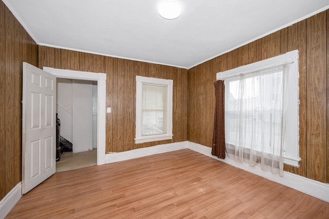 unfurnished room featuring wooden walls, light wood-style flooring, and crown molding