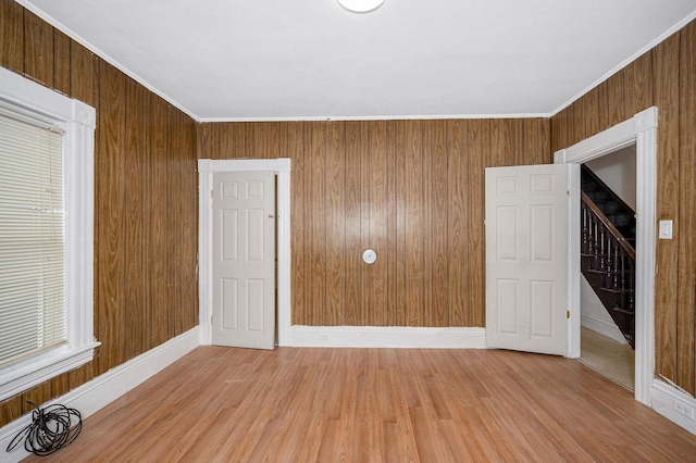 unfurnished room with ornamental molding, light wood-type flooring, wood walls, and stairway