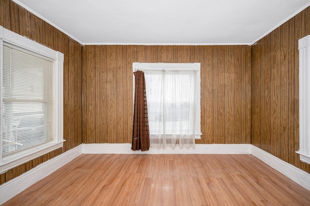 unfurnished room with crown molding, wooden walls, baseboards, and wood finished floors