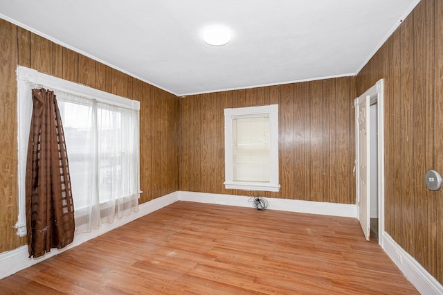 unfurnished room with ornamental molding, wood walls, and light wood finished floors