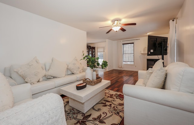 living area with a glass covered fireplace, wood finished floors, a ceiling fan, and baseboards