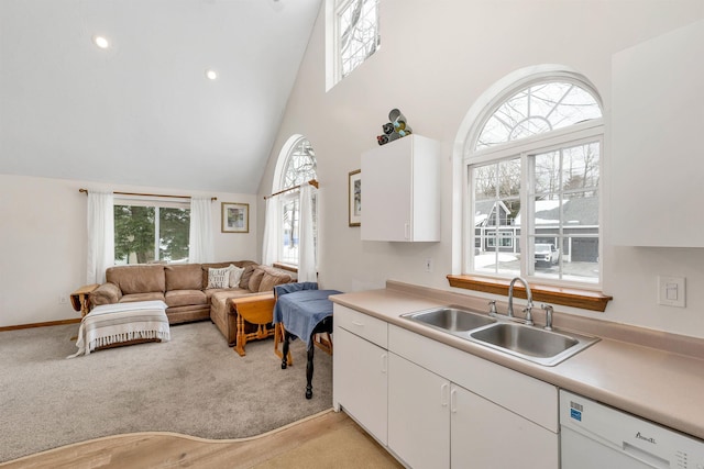 kitchen featuring light countertops, white cabinets, white dishwasher, light carpet, and a sink