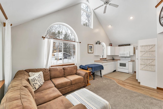 living area featuring light wood-type flooring, high vaulted ceiling, and a ceiling fan