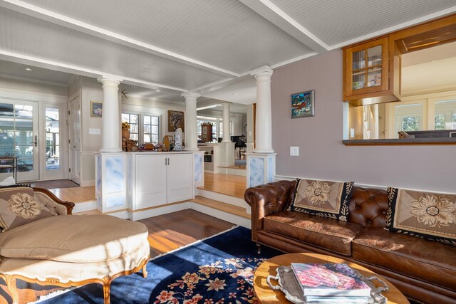 living area with wood finished floors, beam ceiling, and ornate columns