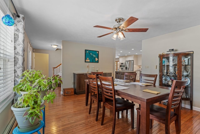 dining room featuring light wood finished floors, baseboards, a ceiling fan, stairway, and a baseboard heating unit