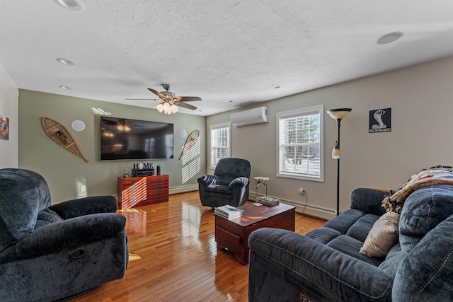 living area featuring baseboard heating, an AC wall unit, a textured ceiling, baseboards, and hardwood / wood-style flooring