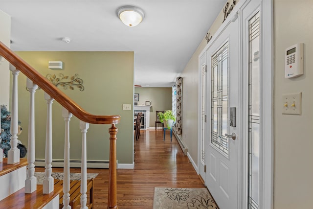 foyer entrance featuring a baseboard heating unit, stairway, baseboards, and wood finished floors