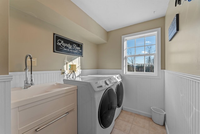 washroom with light tile patterned flooring, a sink, wainscoting, cabinet space, and washer and clothes dryer