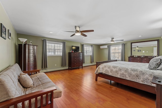 bedroom with multiple windows, baseboard heating, hardwood / wood-style floors, and a wall mounted AC