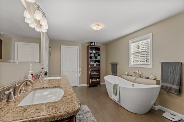 full bathroom with a freestanding bath, wood finished floors, a sink, and baseboards