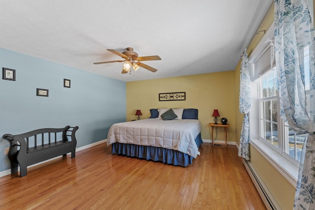 bedroom with light wood-type flooring, baseboards, a baseboard heating unit, and a ceiling fan