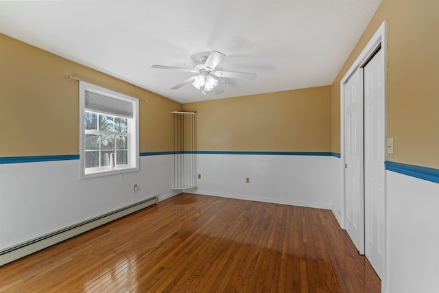 empty room with a baseboard heating unit, wood-type flooring, baseboards, and a ceiling fan