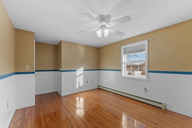 spare room featuring hardwood / wood-style flooring, ceiling fan, a baseboard heating unit, and baseboards