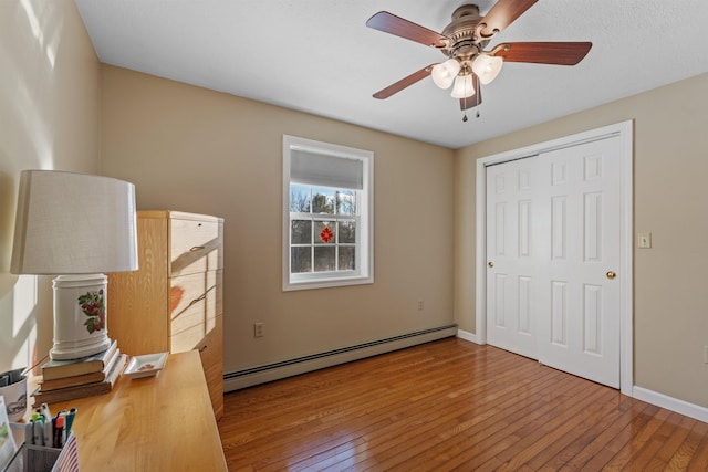 bedroom featuring a baseboard heating unit, a closet, baseboards, and hardwood / wood-style floors