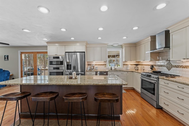 kitchen featuring stainless steel appliances, a sink, a center island, wall chimney exhaust hood, and plenty of natural light