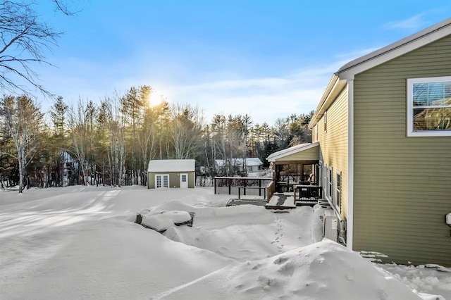 yard layered in snow with a wooden deck, a storage unit, and an outdoor structure