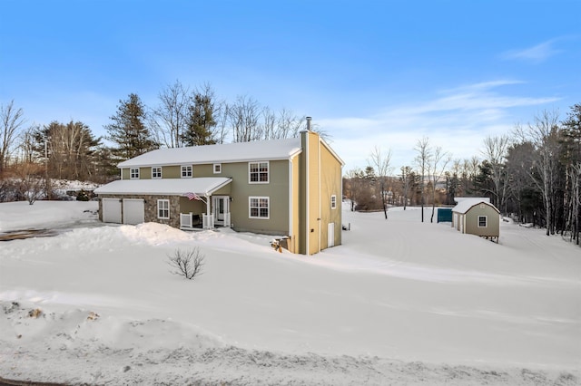 snow covered rear of property with a garage, a chimney, and an outbuilding