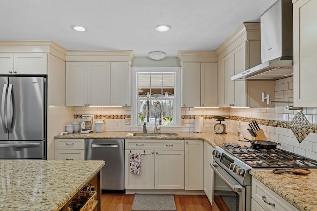 kitchen featuring light stone counters, tasteful backsplash, appliances with stainless steel finishes, a sink, and wall chimney exhaust hood