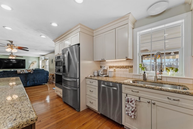 kitchen with backsplash, appliances with stainless steel finishes, open floor plan, a sink, and light wood-type flooring