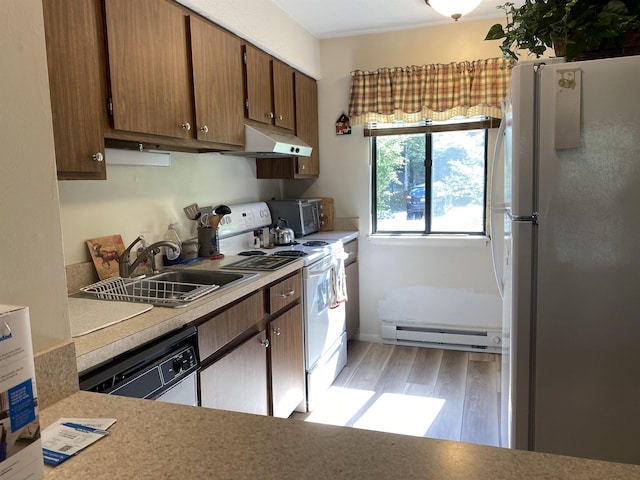 kitchen featuring under cabinet range hood, a baseboard heating unit, white appliances, a sink, and light countertops