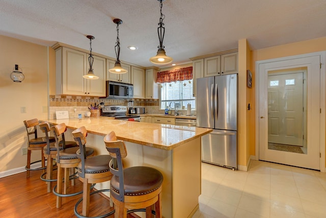 kitchen featuring a breakfast bar, tasteful backsplash, hanging light fixtures, appliances with stainless steel finishes, and a peninsula