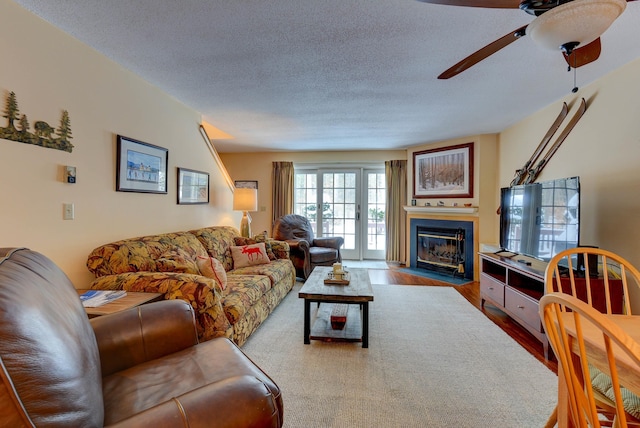 living area featuring a fireplace with flush hearth, a textured ceiling, a ceiling fan, and wood finished floors