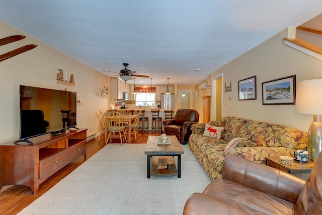 living area featuring baseboard heating, a ceiling fan, and light wood-style floors