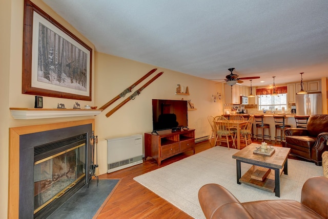 living area featuring a baseboard radiator, a fireplace with flush hearth, a ceiling fan, and light wood-style floors