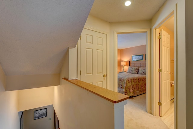 hallway featuring light colored carpet, a textured ceiling, and an upstairs landing