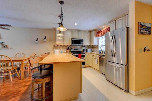 kitchen featuring a peninsula, stainless steel appliances, cream cabinetry, light countertops, and a kitchen bar