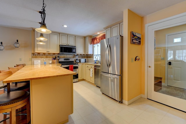 kitchen with a peninsula, cream cabinets, stainless steel appliances, light countertops, and a sink