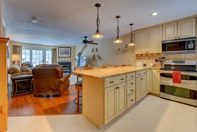 kitchen with a glass covered fireplace, a breakfast bar area, open floor plan, cream cabinets, and stainless steel appliances