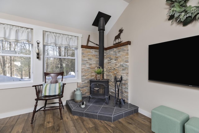 living area with lofted ceiling, wood finished floors, a wood stove, and baseboards