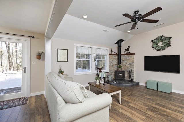 living area featuring wood-type flooring, visible vents, a wood stove, vaulted ceiling, and baseboards