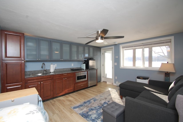 kitchen featuring stainless steel appliances, a sink, light wood-style floors, dark stone countertops, and glass insert cabinets