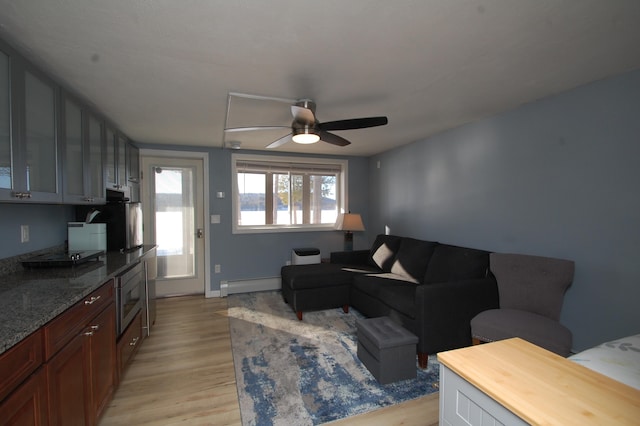 living room featuring a baseboard heating unit, light wood-style floors, plenty of natural light, and ceiling fan