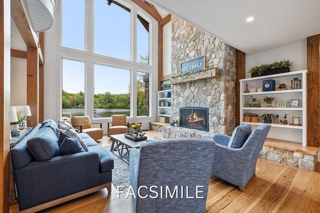 living area featuring a towering ceiling, built in shelves, wood finished floors, and a stone fireplace