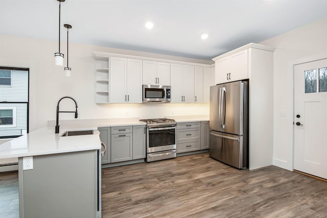 kitchen with appliances with stainless steel finishes, wood finished floors, a peninsula, open shelves, and a sink