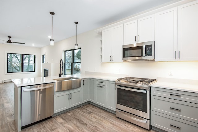 kitchen featuring open shelves, stainless steel appliances, gray cabinetry, a sink, and a peninsula