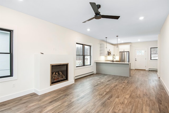 unfurnished living room featuring baseboard heating, a sink, and wood finished floors