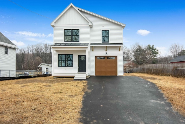 view of front of property featuring metal roof, an attached garage, fence, driveway, and a standing seam roof