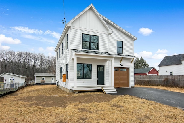 modern farmhouse style home featuring board and batten siding, a standing seam roof, driveway, and fence