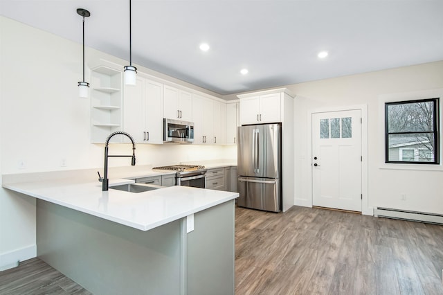 kitchen featuring appliances with stainless steel finishes, wood finished floors, a peninsula, open shelves, and a sink