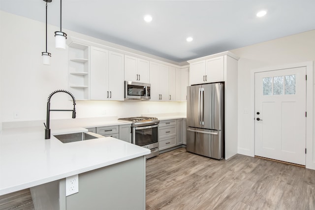 kitchen featuring open shelves, stainless steel appliances, a sink, light wood-type flooring, and a peninsula