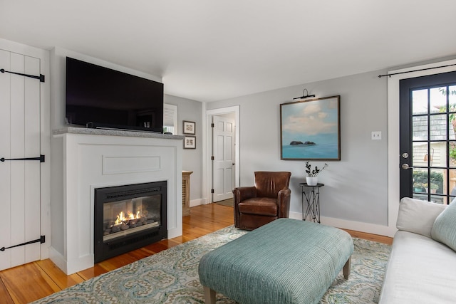 living area featuring light wood-style flooring, baseboards, and a glass covered fireplace