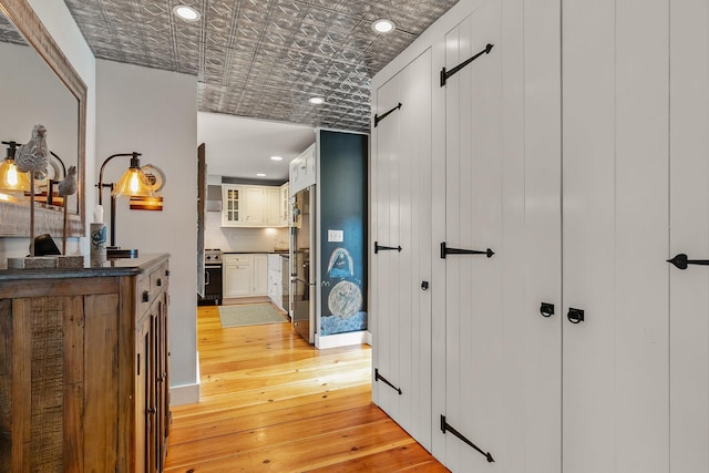 hallway featuring a barn door, light wood-type flooring, an ornate ceiling, and recessed lighting