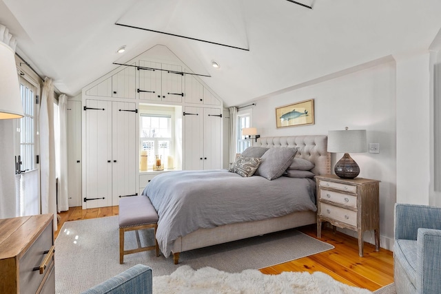 bedroom featuring multiple closets, lofted ceiling, and light wood-style flooring