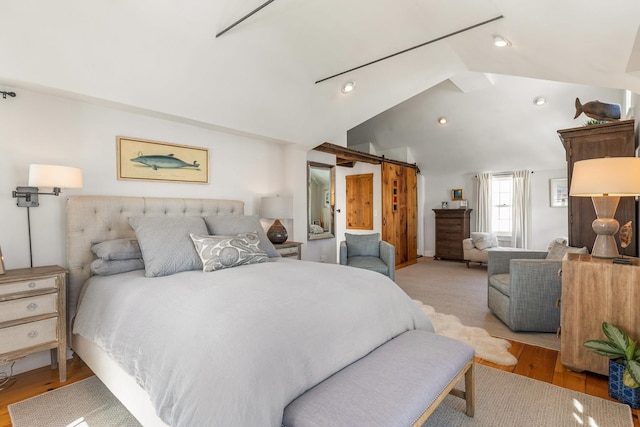 bedroom featuring lofted ceiling, light wood finished floors, and a barn door